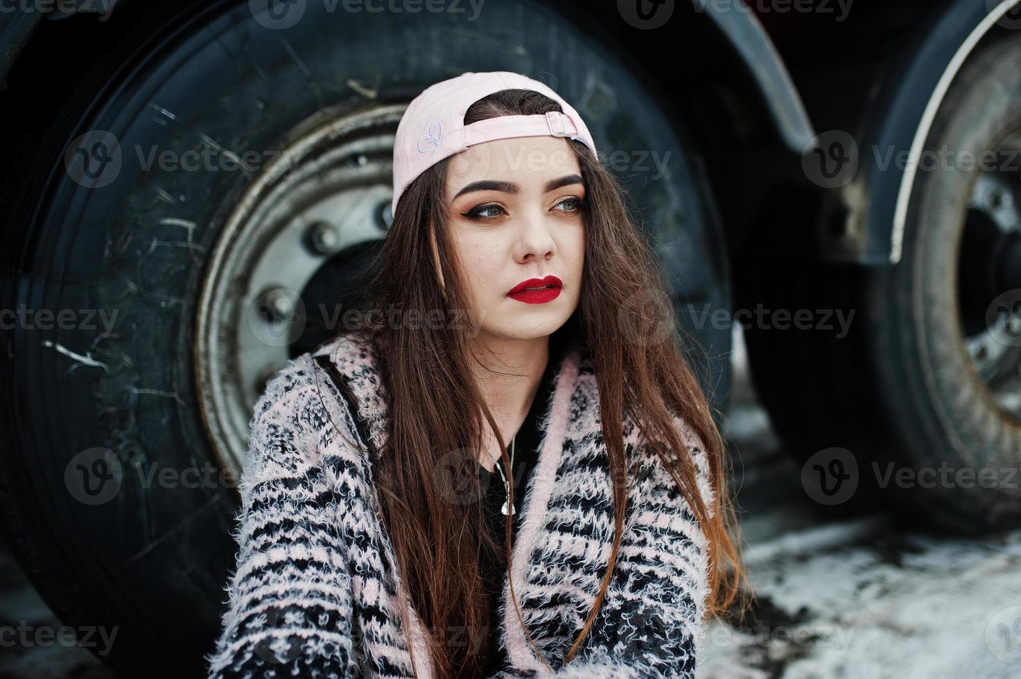 chica casual elegante morena con gorra sentada contra las ruedas del camión. foto