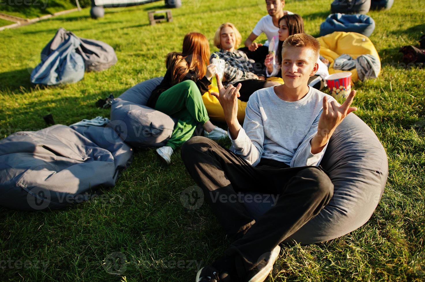 Young multi ethnic group of people watching movie at poof in open air cinema. Close up portrait of funny guy. photo