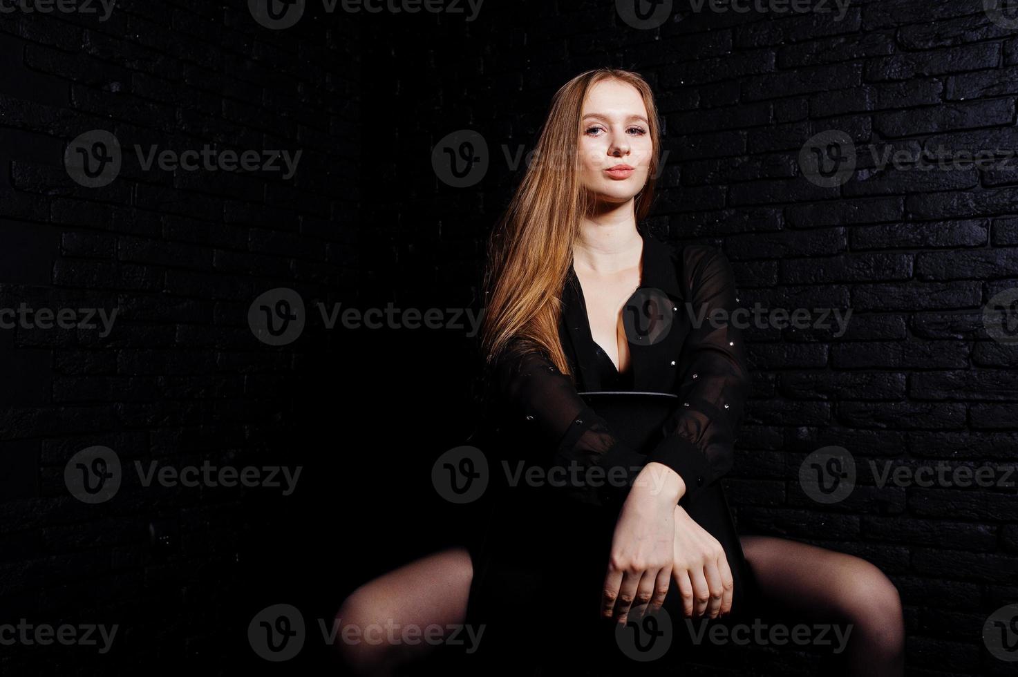 Studio shot of brunette girl in black blouse with bra and shorts against black brick wall. photo