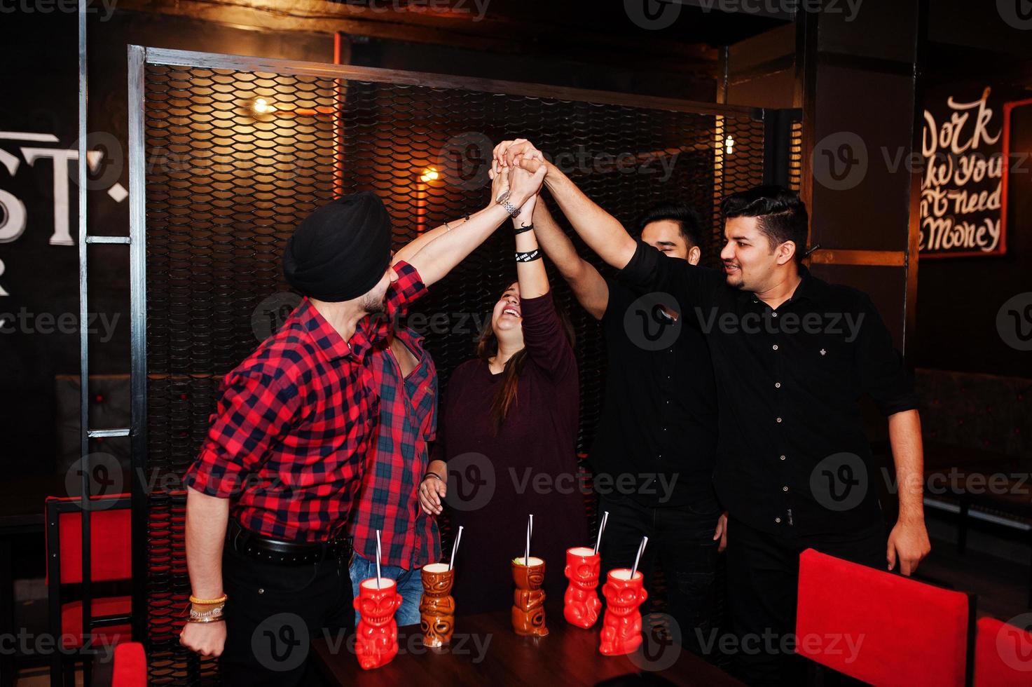 grupo de amigos indios divirtiéndose y descansando en el club nocturno, bebiendo cócteles y dando cinco juntos. foto