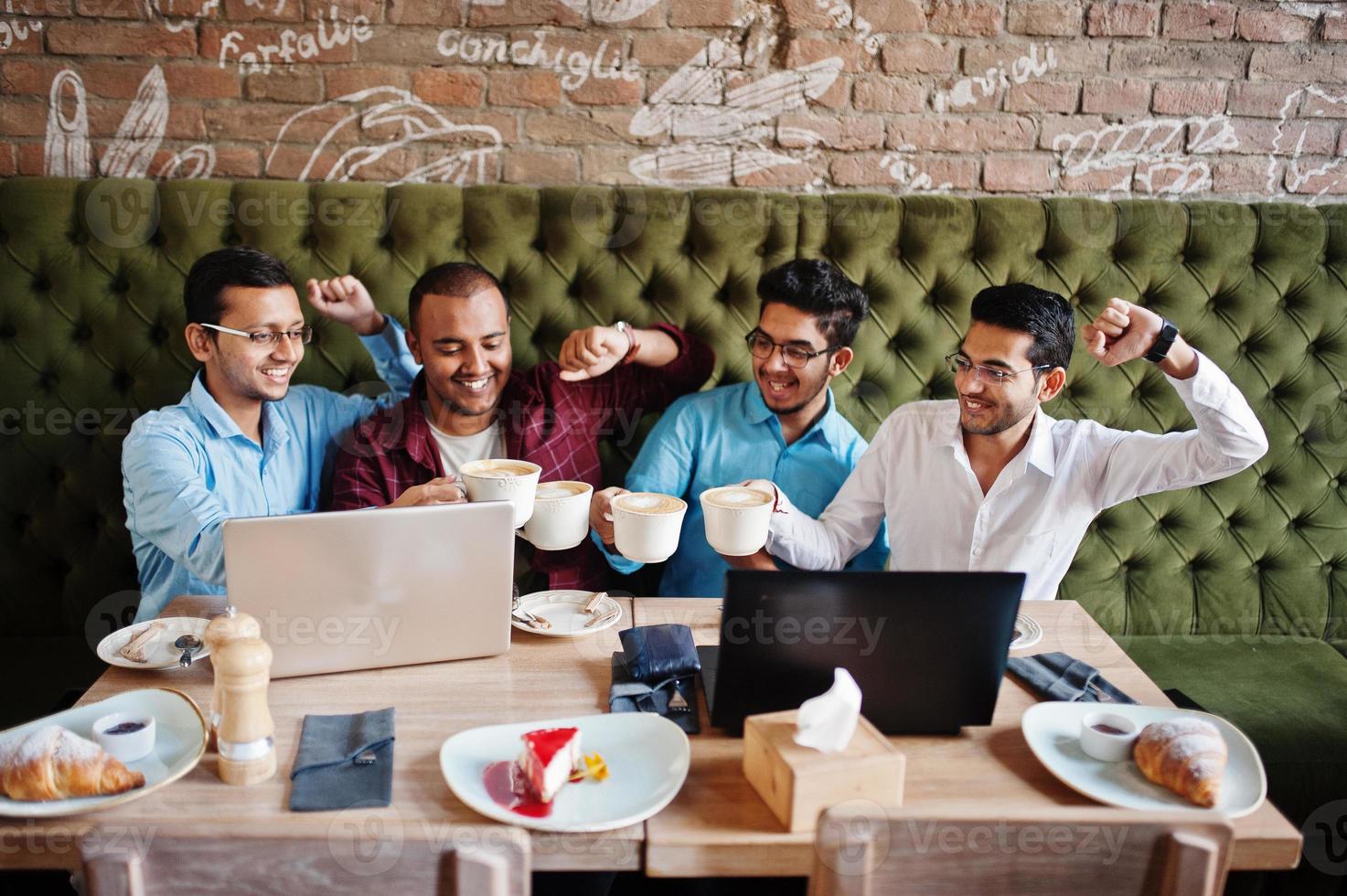 Group of four south asian men's posed at business meeting in cafe. Indians work with laptops together using various gadgets, having conversation and drink coffee. photo