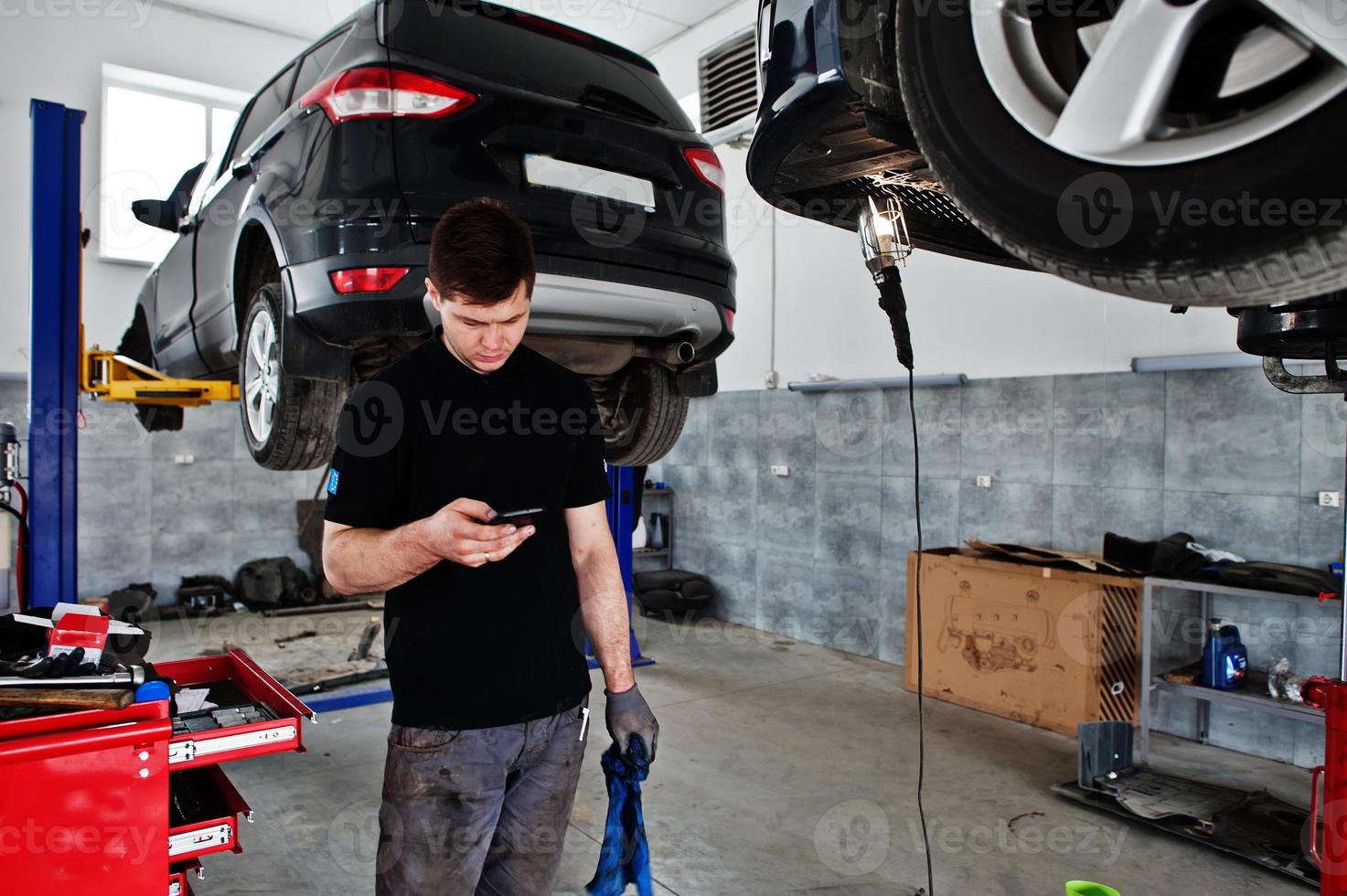 Car repair and maintenance theme. Mechanic in uniform working in auto service, using mobile phone. photo