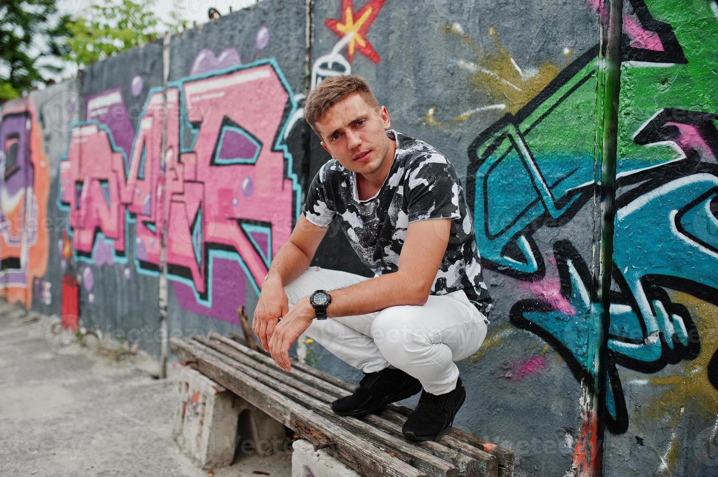 Lifestyle portrait of handsome man posing on the street of city with graffiti wall. photo