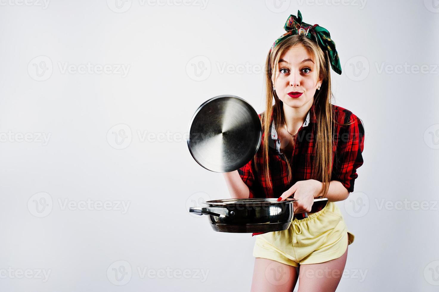 Young funny housewife in checkered shirt and yellow shorts pin up style with frying pan isolated on white background. photo