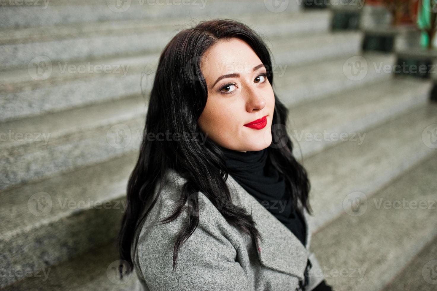 Brunette girl in gray coat posed in stairs of railway station indoor. photo