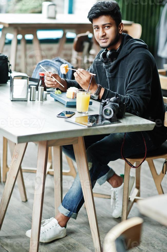 Casual and stylish young asian man with earphones at cafe eating sushi. photo