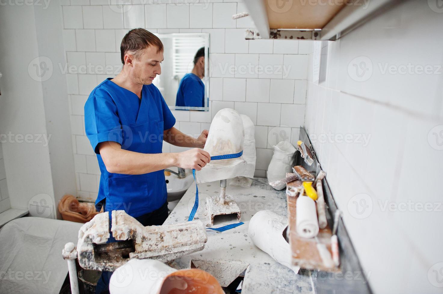 Prosthetist man making prosthetic leg while working in laboratory, makes a model of plaster. photo