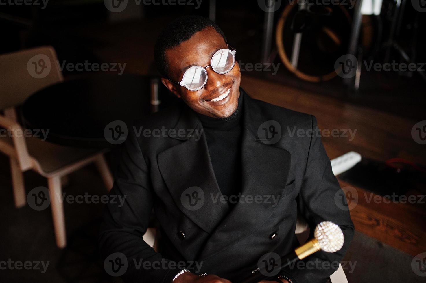 Stylish african american gentleman in elegant black jacket and glasses, holding retro walking stick as cane flask or tippling cane with golden diamond ball handle. Rich fashionable afro man. photo