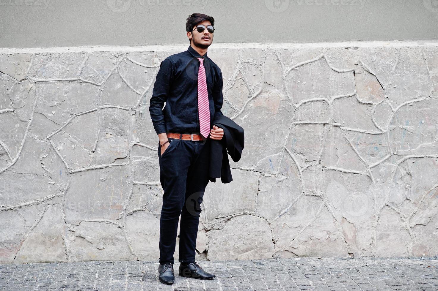 Young indian man on black shirt, tie and sunglasses posed outdoor. photo