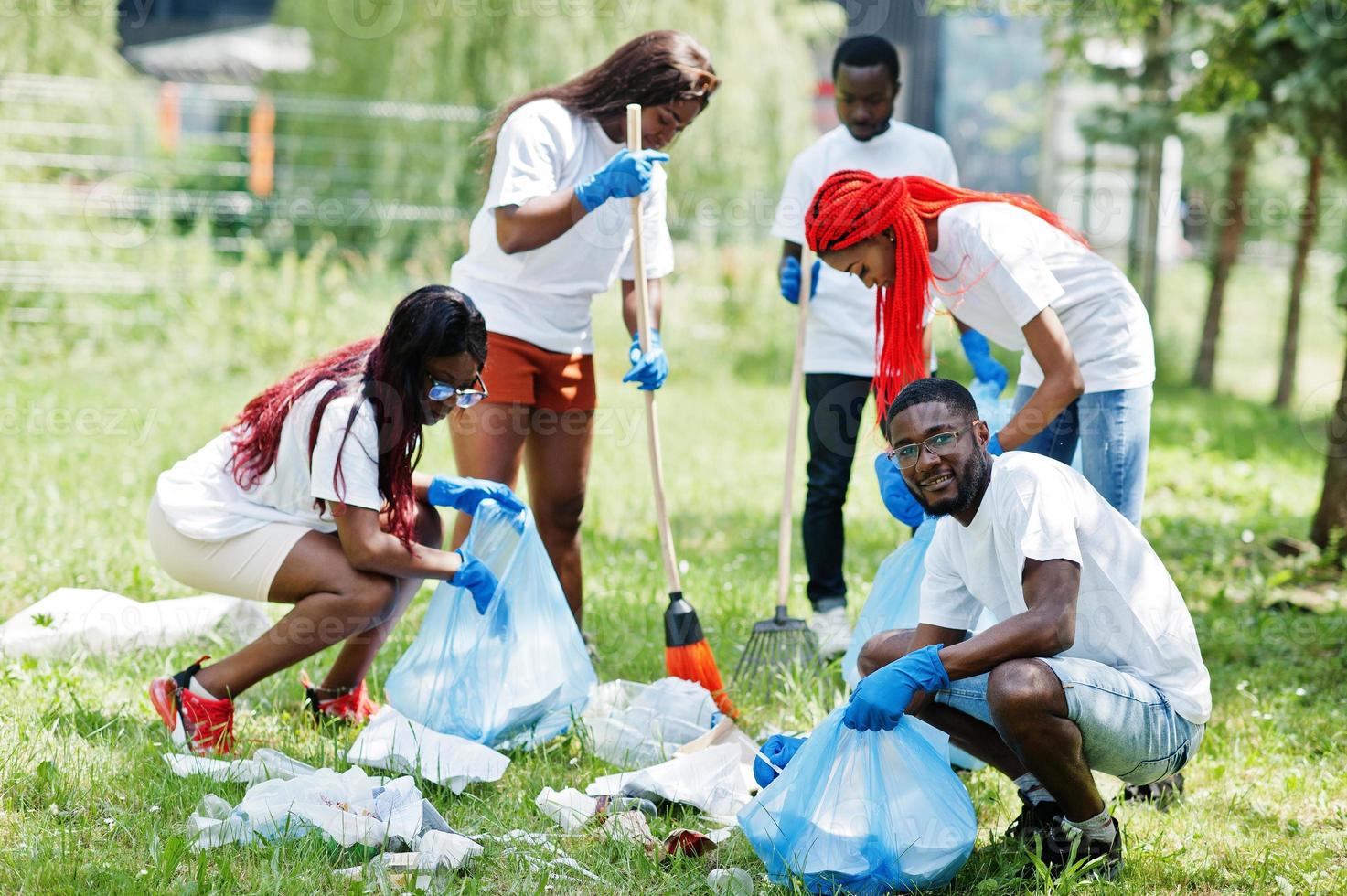 Group of happy african volunteers with garbage bags cleaning area in park. Africa volunteering, charity, people and ecology concept. photo