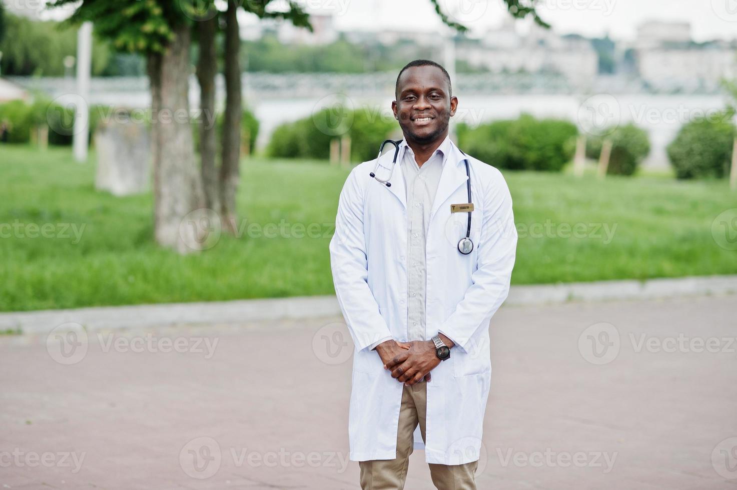 joven médico afroamericano de bata blanca con un estetoscopio posado al aire libre. foto