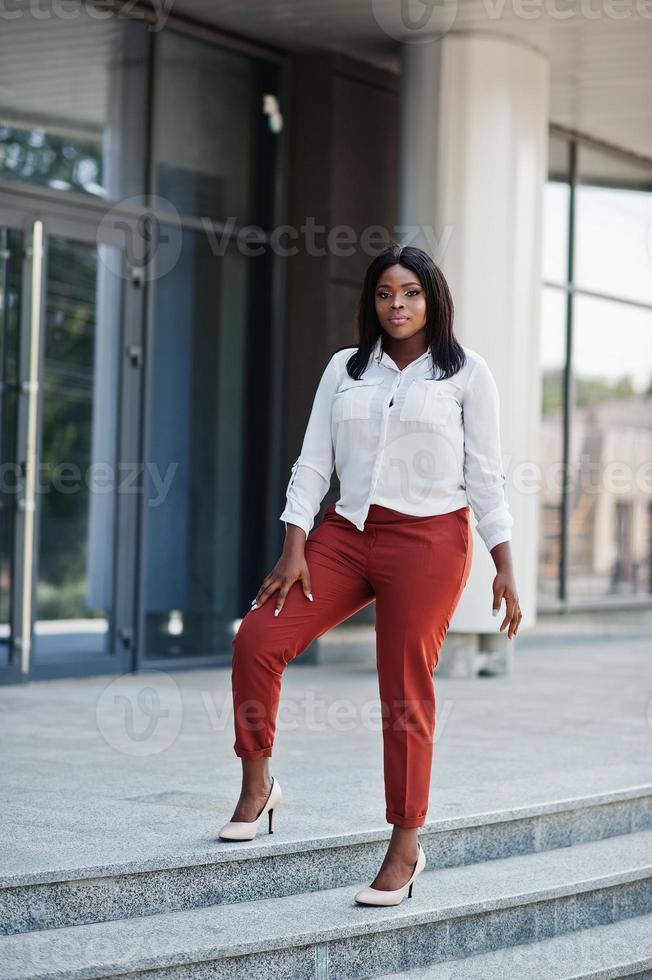 Formally dressed african american business woman in white blouse and red trousers. Successful dark skinned businesswoman. photo