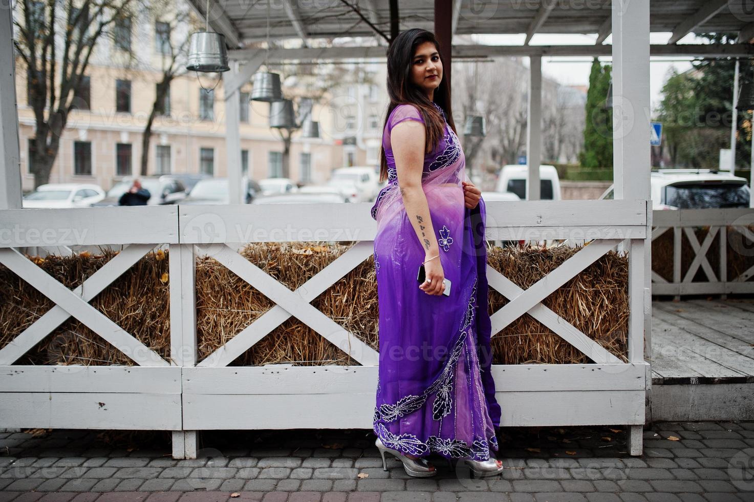Indian hindu girl at traditional violet saree posed at street against wooden terrace. photo