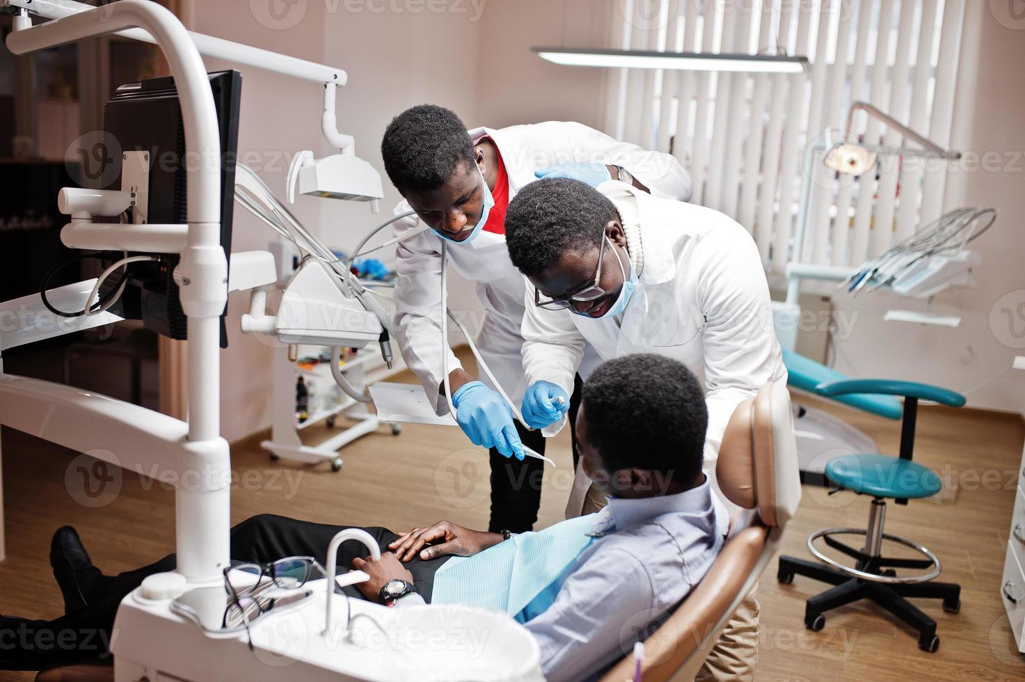 paciente afroamericano en silla dental. oficina de dentista y concepto de práctica médica. dentista profesional ayudando a su paciente en odontología médica. taladrar los dientes del paciente en la clínica. foto