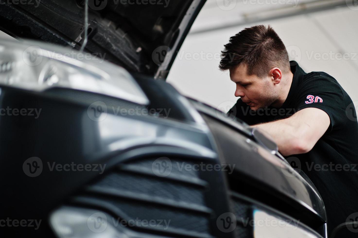 Car repair and maintenance theme. Mechanic in uniform working in auto service, checking engine. photo