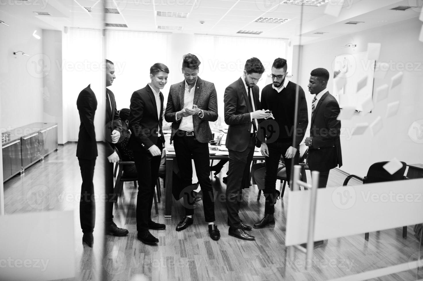 Six multiracial business mans standing at office and use mobile phones. Diverse group of male employees in formal wear with cellphones. photo