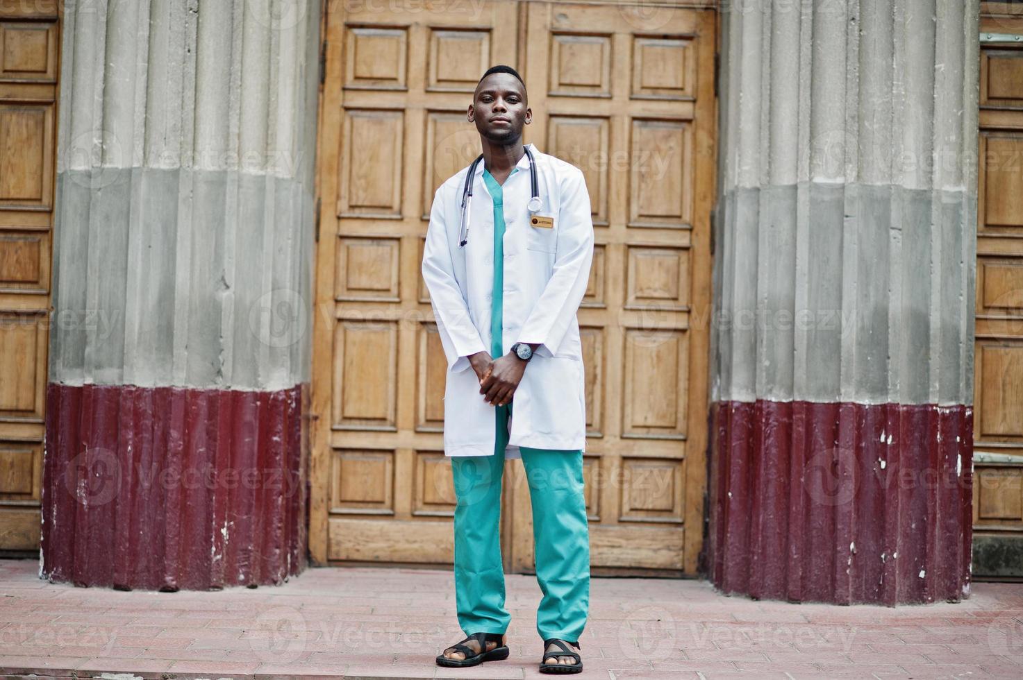 African american doctor male at lab coat with stethoscope outdoor against clinic door. photo