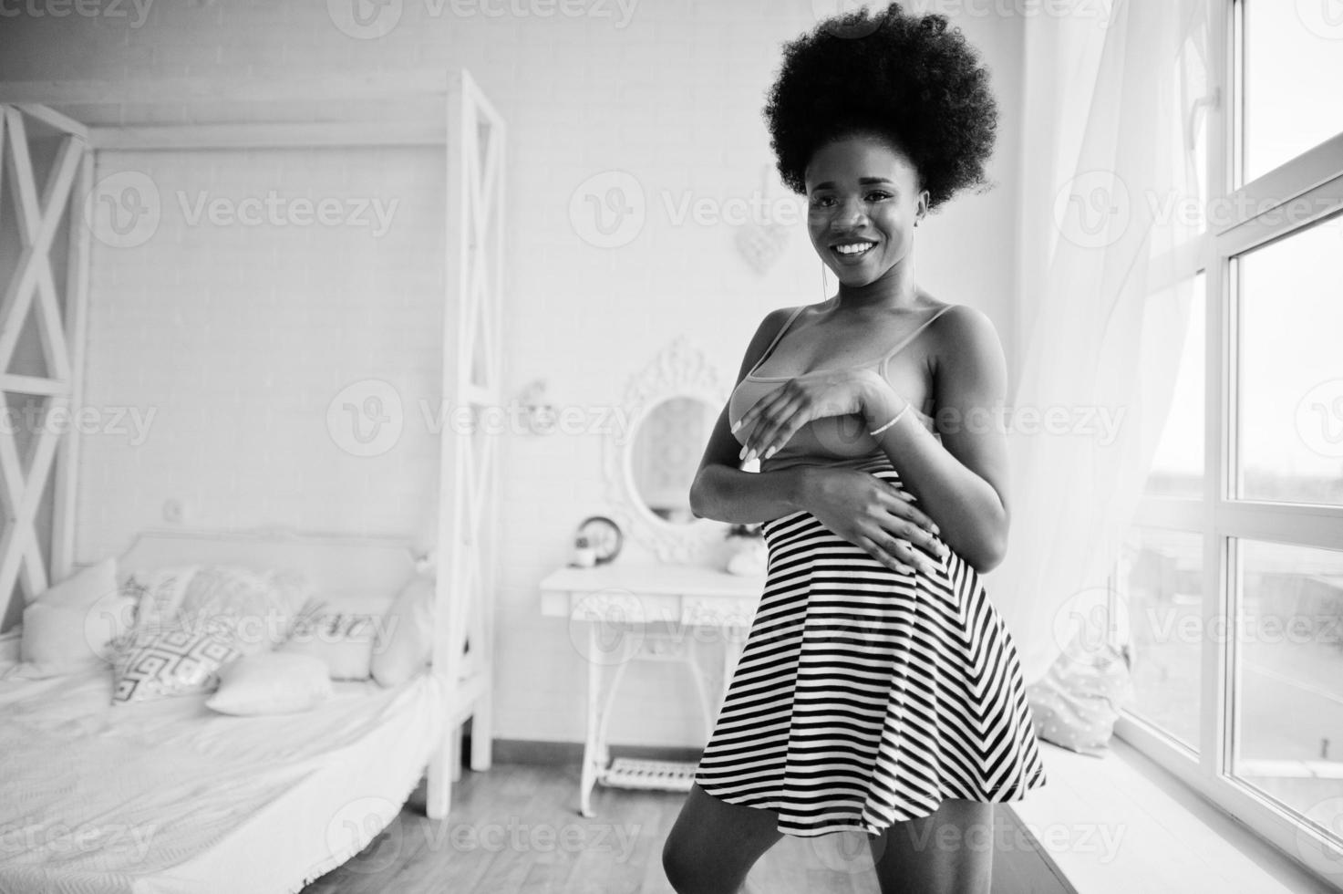 Attractive african american woman with afro hair wear on skirt pink top, posed at white room. Fashionable sexy black model. photo