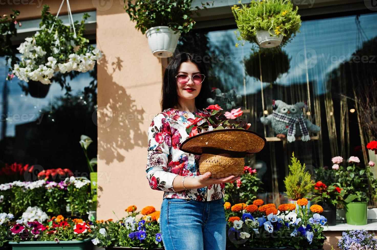 Summer portrait of brunette girl in pink glasses and hat against flowers shop. photo