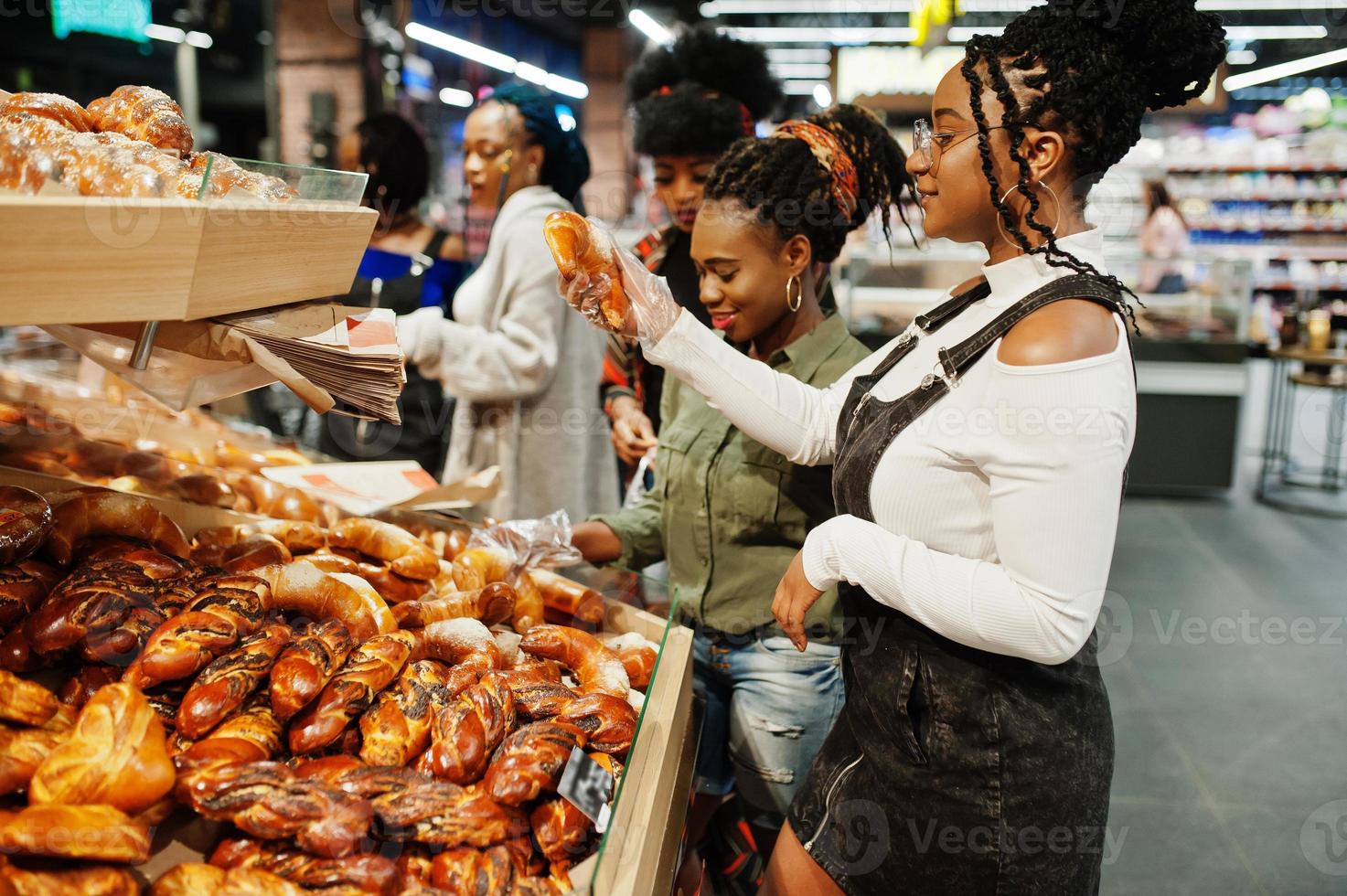 Group of african womans with shopping carts near baked products at a supermarket. photo