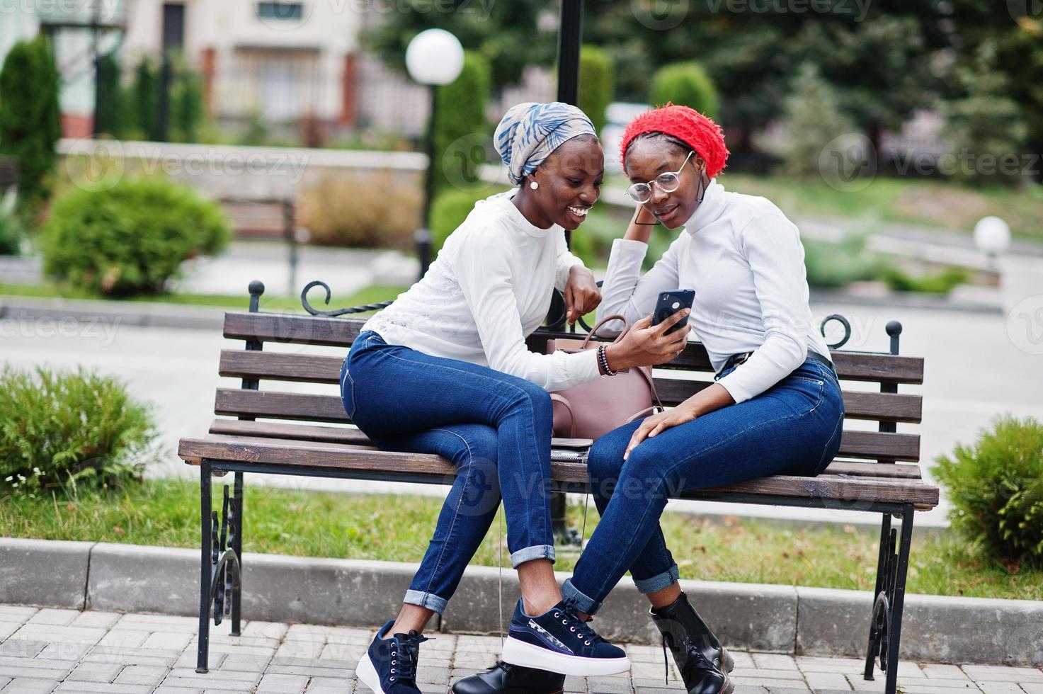 Two young modern fashionable, attractive, tall and slim african muslim womans in hijab or turban head scarf posed together with mobile phones at hands. photo