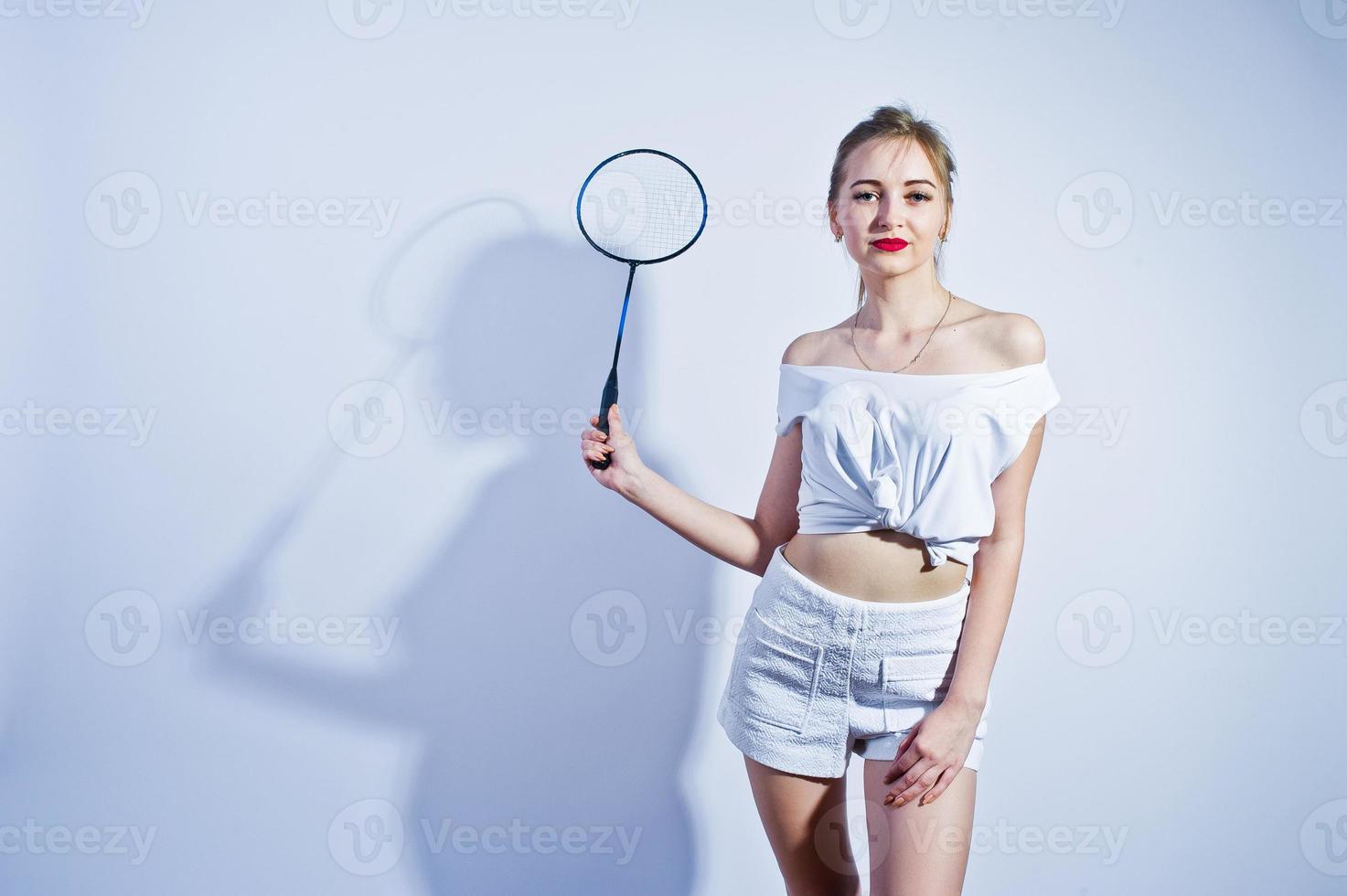Amazing fit sexy body brunette caucasian girl posing at studio against white background on shorts and top with badminton racket. photo