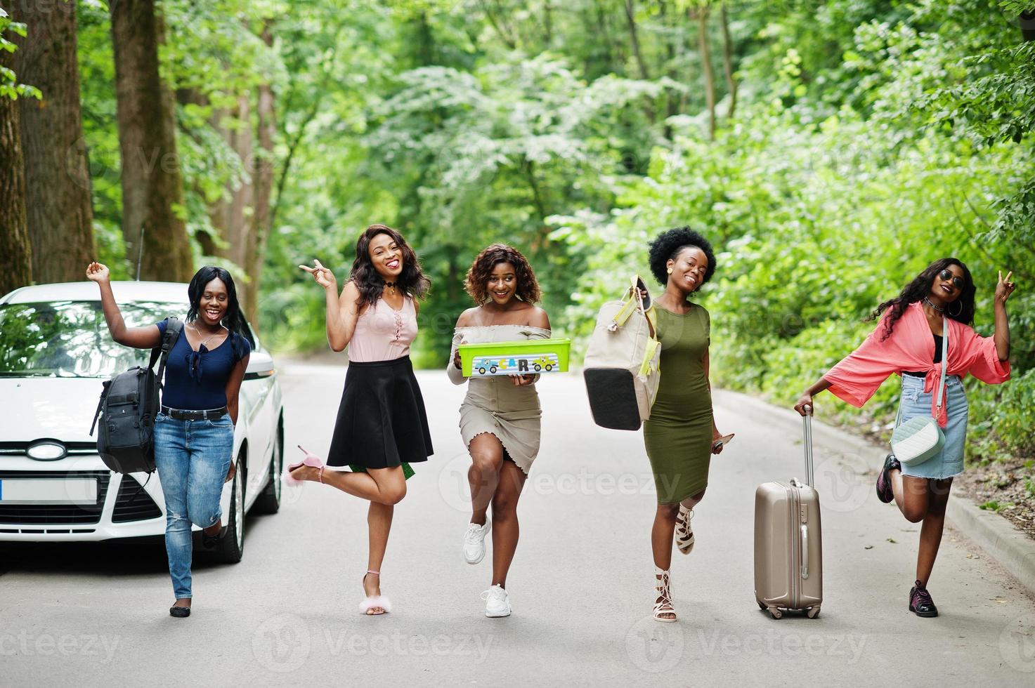 Group of five happy african american traveler girls walking with bags against car. photo