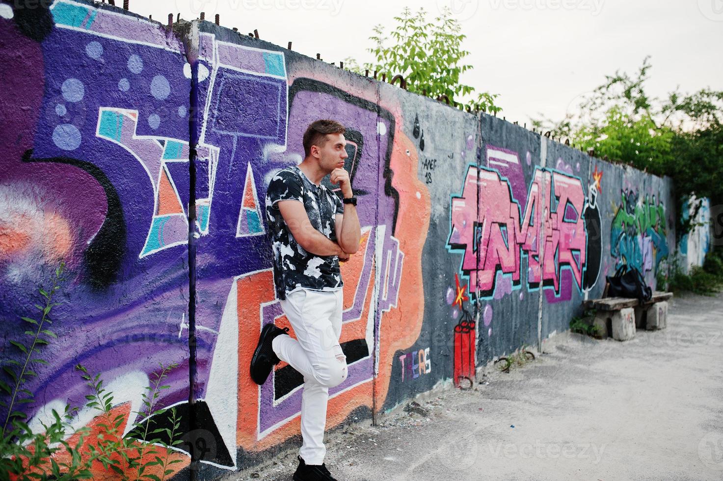 retrato de estilo de vida de un hombre guapo posando en la calle de la ciudad con una pared de graffiti. foto