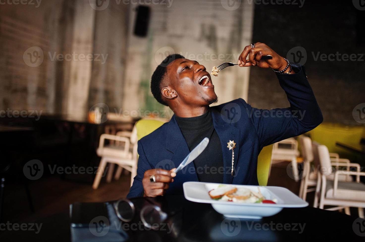 Fashionable african american man in suit sitting at cafe and eating salad. photo