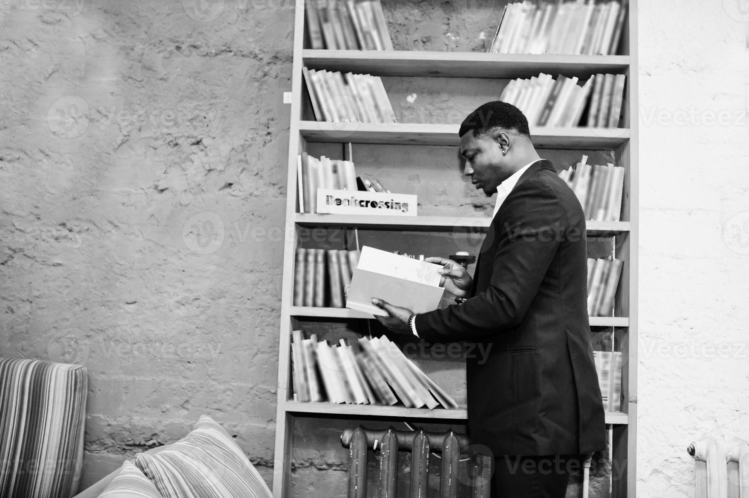 Strong powerful african american man in black suit read book against shelves in free books anti cafe. photo