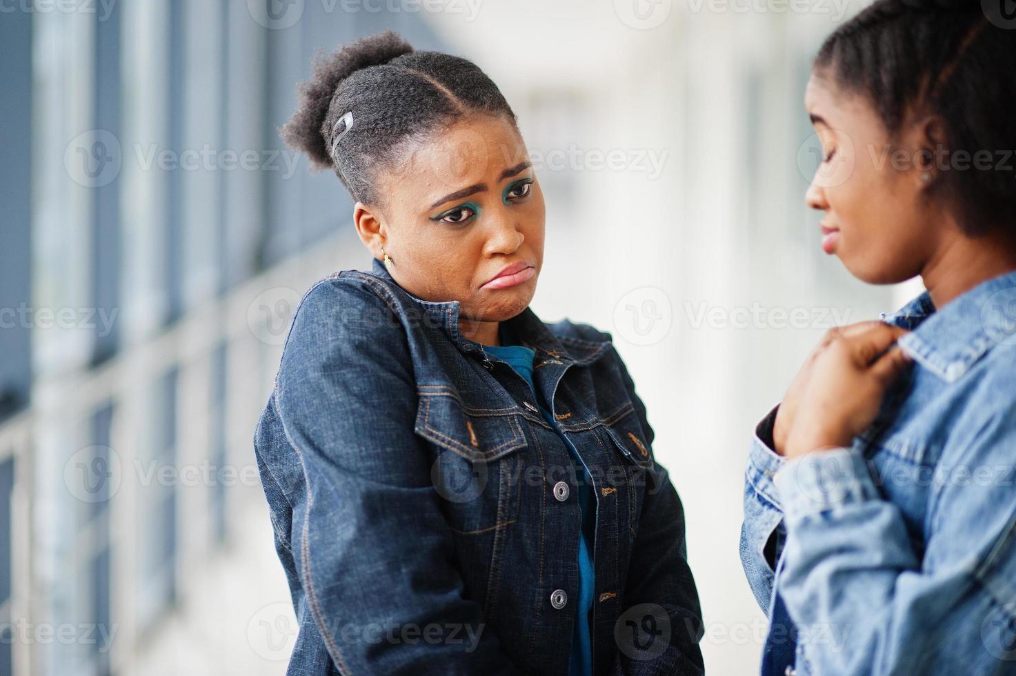 dos amigas africanas con caras tristes en chaqueta de jeans posaron juntas en el interior. foto