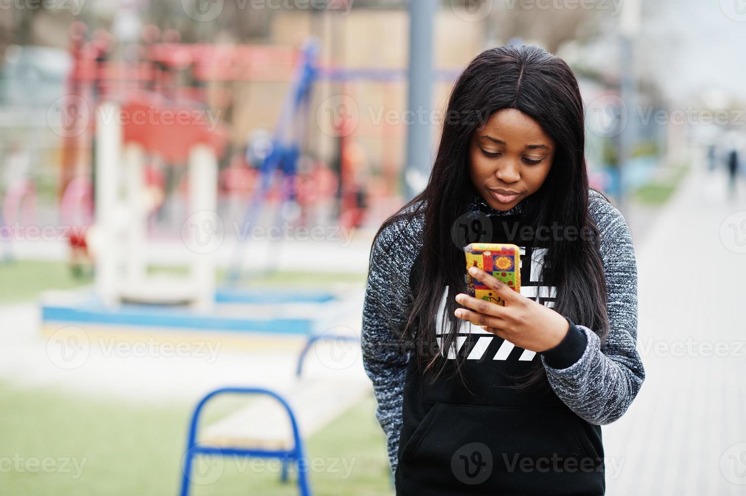 Young millennial african american girl in city. Happy black woman with mobile phone. Generation Z concept. photo