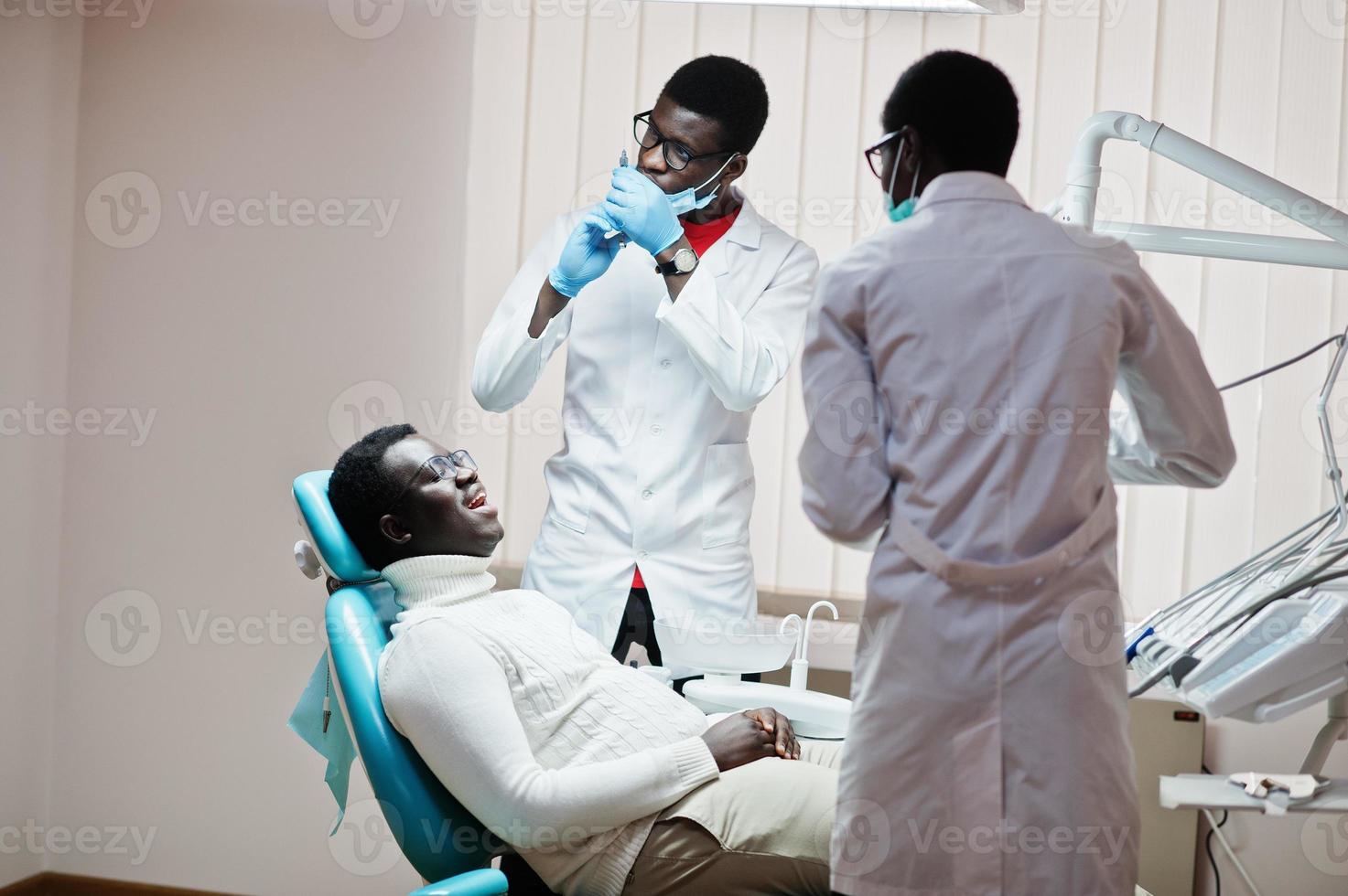 paciente afroamericano en silla dental. oficina de dentista y concepto de práctica médica. dentista profesional ayudando a su paciente en odontología médica. anestésico de inyección. foto