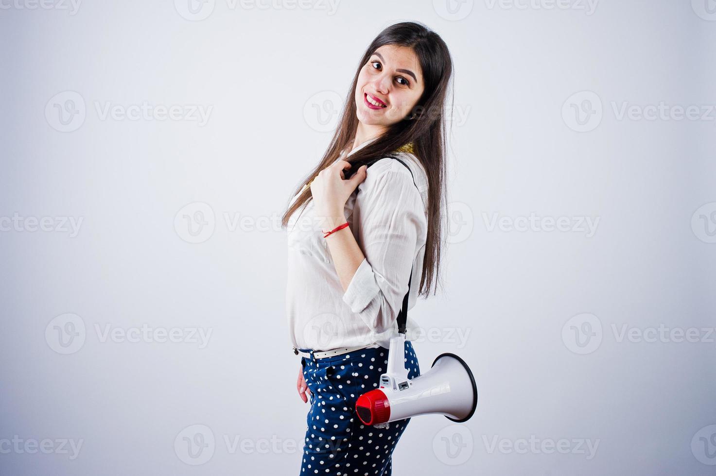 retrato de una mujer joven con pantalones azules y blusa blanca posando con megáfono en el estudio. foto