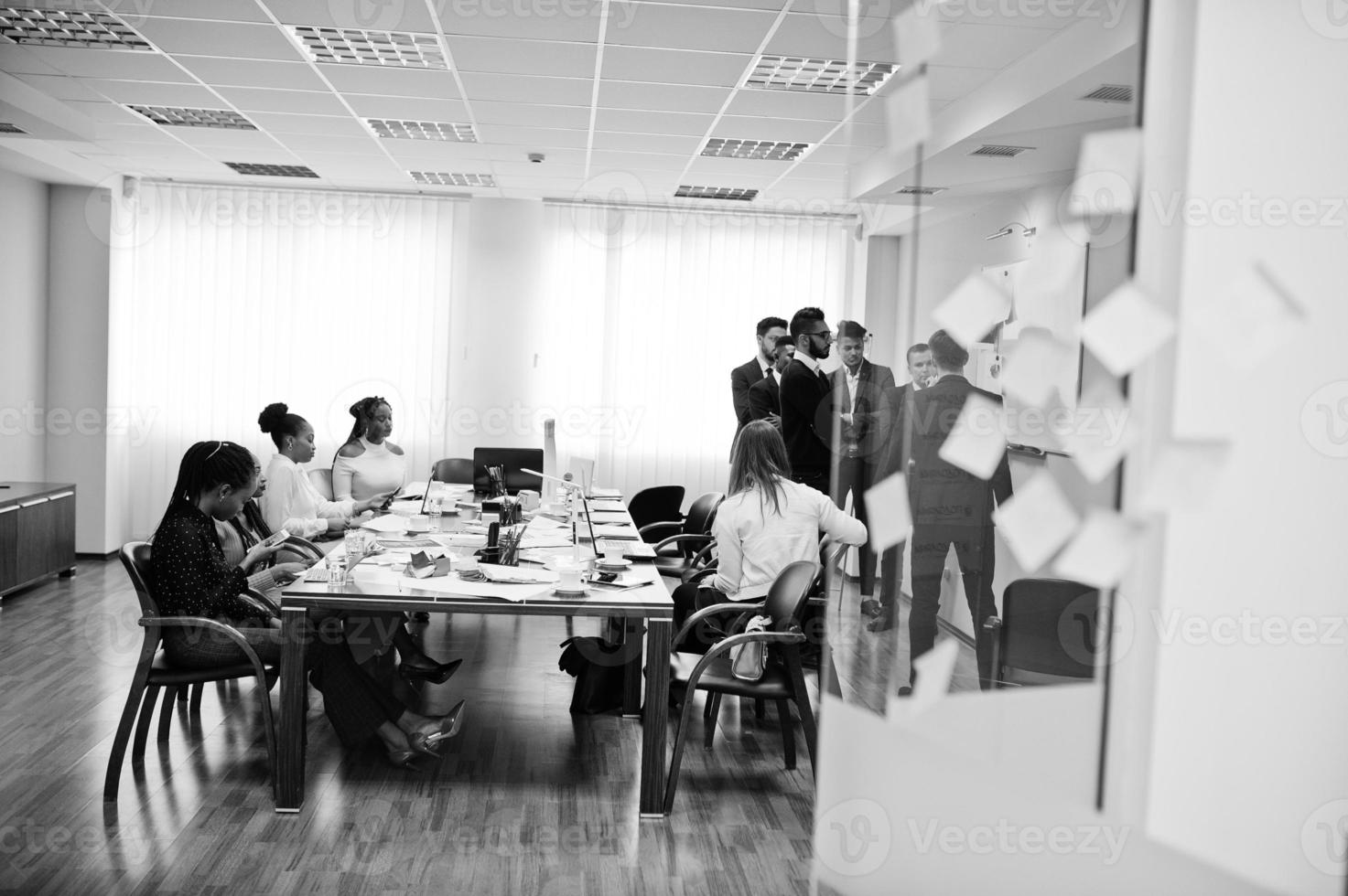 Multiracial business team addressing meeting around boardroom table and write plan on board. photo