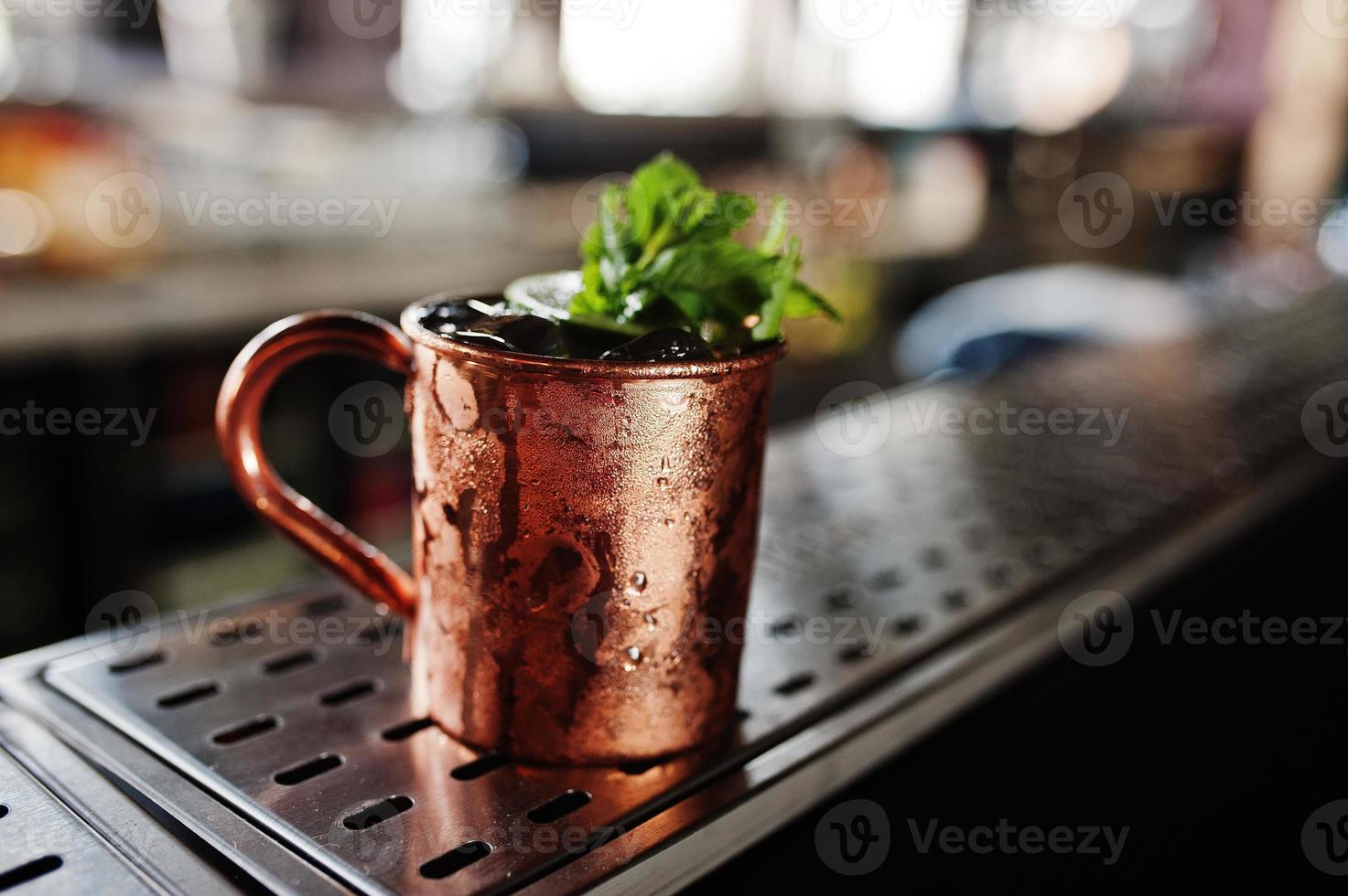 Alcoholic cocktail with ice, mint and lime in bronze cup on bar table. photo