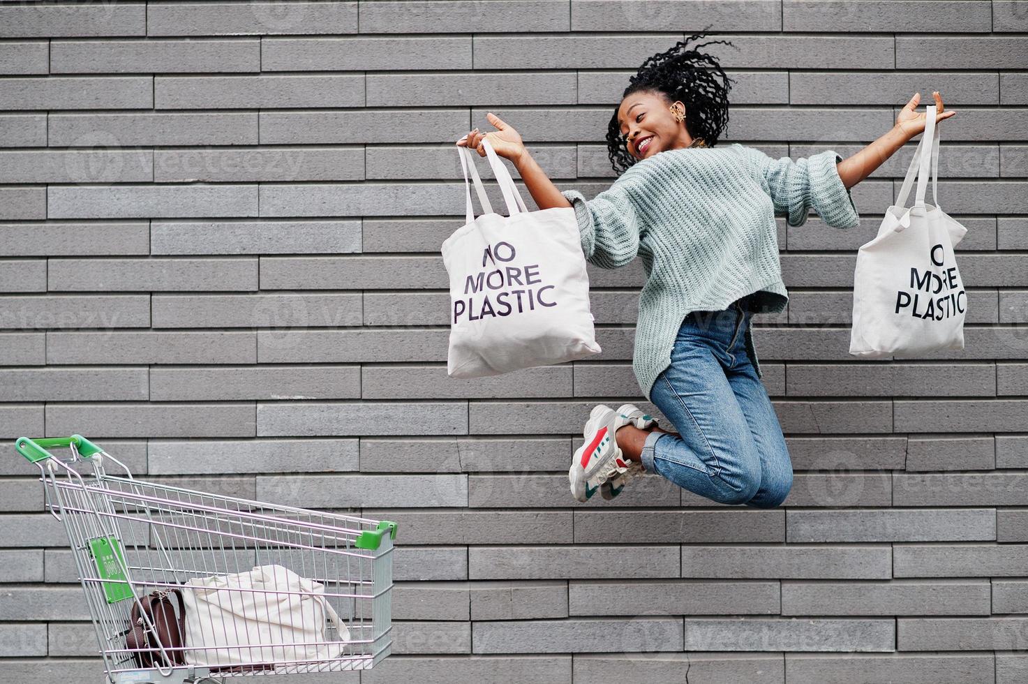 No more plastic. African woman with shopping cart trolley and eco bags jump outdoor market. photo