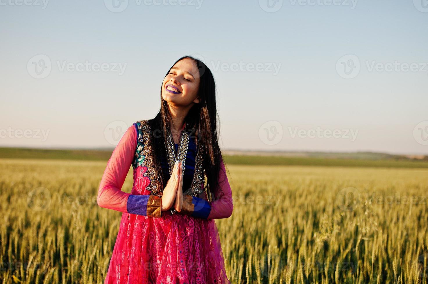 tierna niña india en sari, con maquillaje de labios violetas posada en el campo al atardecer. modelo indio de moda. foto