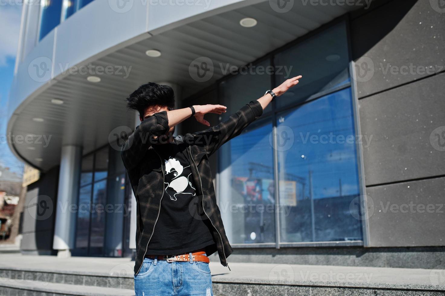 Beard asian man in casual wear posing against new modern building and show dab. photo