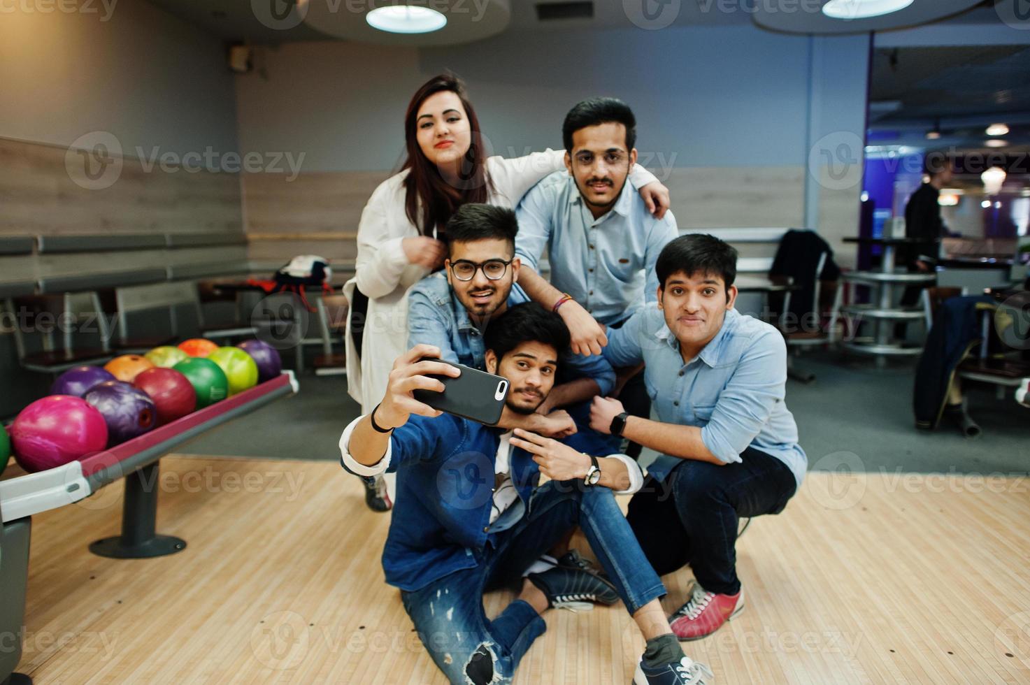 Group of five south asian peoples having rest and fun at bowling club. Making selfie by phone. photo