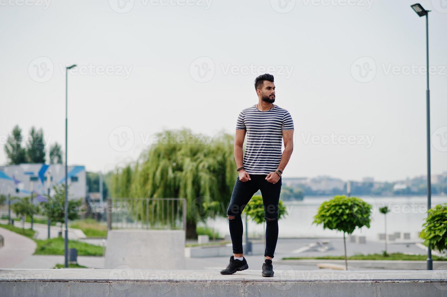 apuesto modelo de hombre de barba árabe alto en camisa desnuda posada al aire libre en el parque de patinaje. chico árabe de moda. foto