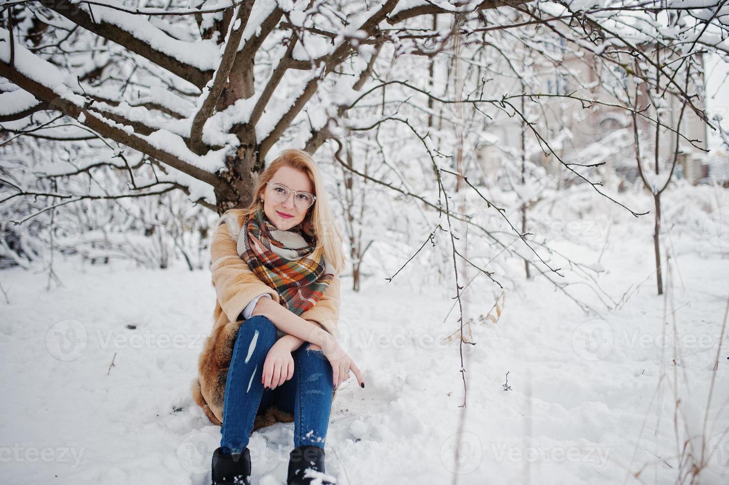 Portraiy of blonde girl in glasses, red fur coat and scarf at winter day. photo