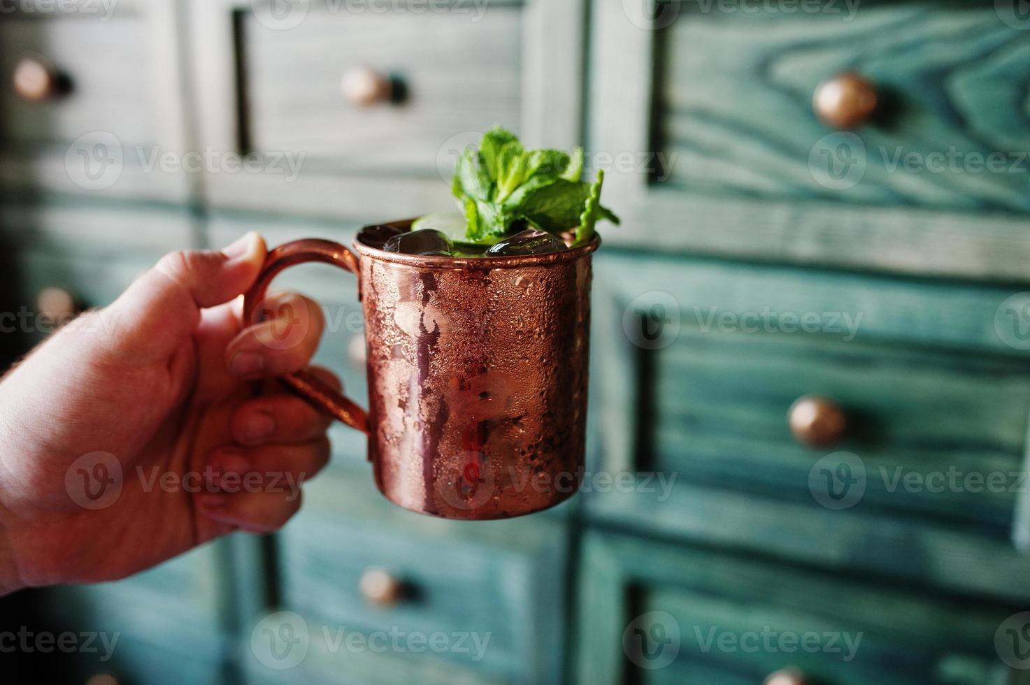 Alcoholic cocktail with ice, mint and lime in bronze cup at hand of barman. photo