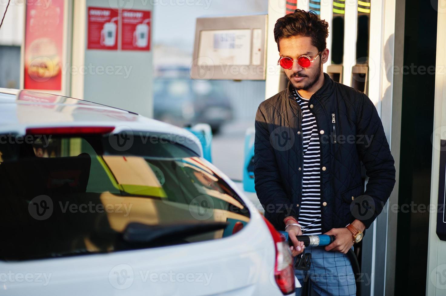 hombre del sur de asia o hombre indio repostando su auto blanco en la gasolinera. foto