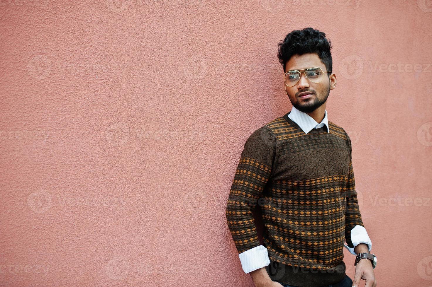 Portrait of young stylish indian man model in eyeglasses isolated on pink wall background. photo