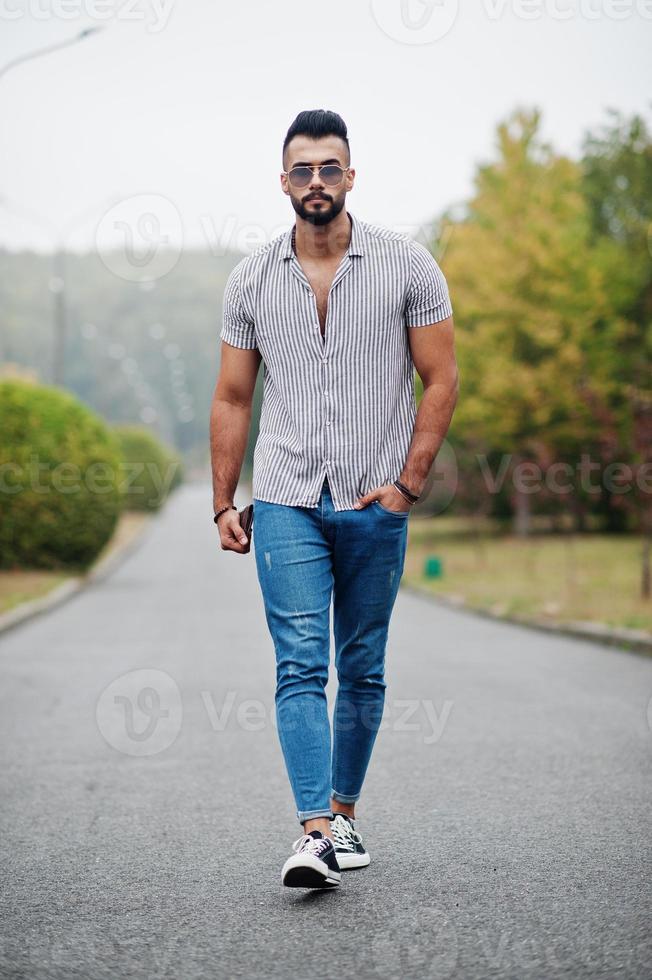 Fashionable tall arab beard man wear on shirt, jeans and sunglasses posed on park and hold wallet at hand. photo