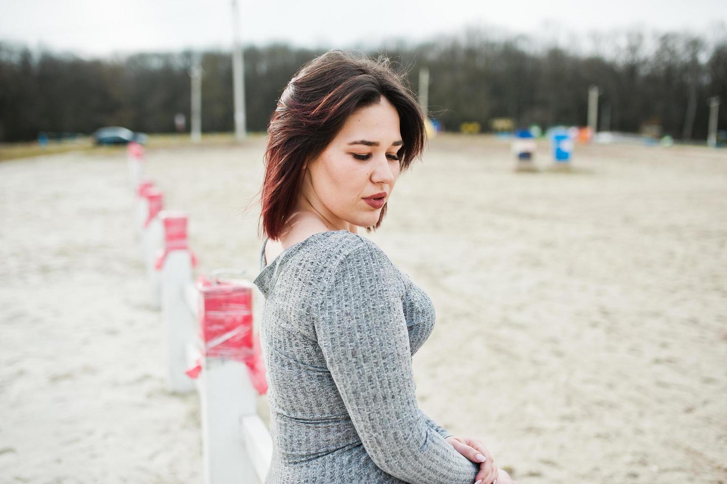 Portrait of brunette girl in gray dress sitting at white wooden construction. photo