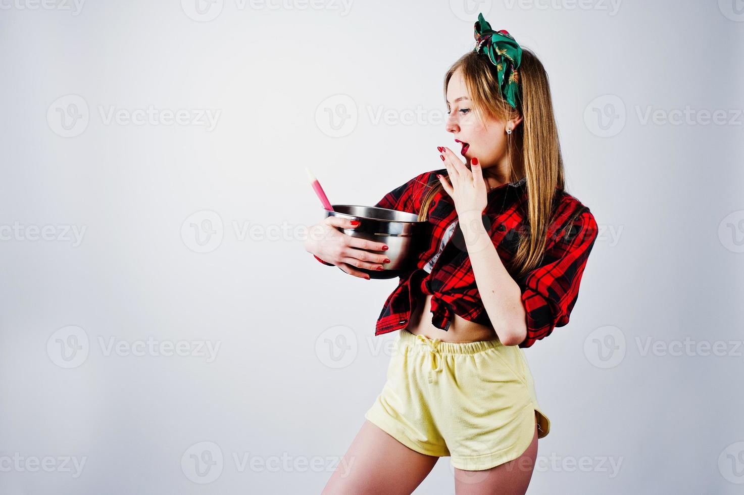 Young funny housewife in checkered shirt and yellow shorts pin up style with saucepan and kitchen spoon isolated on white background. photo