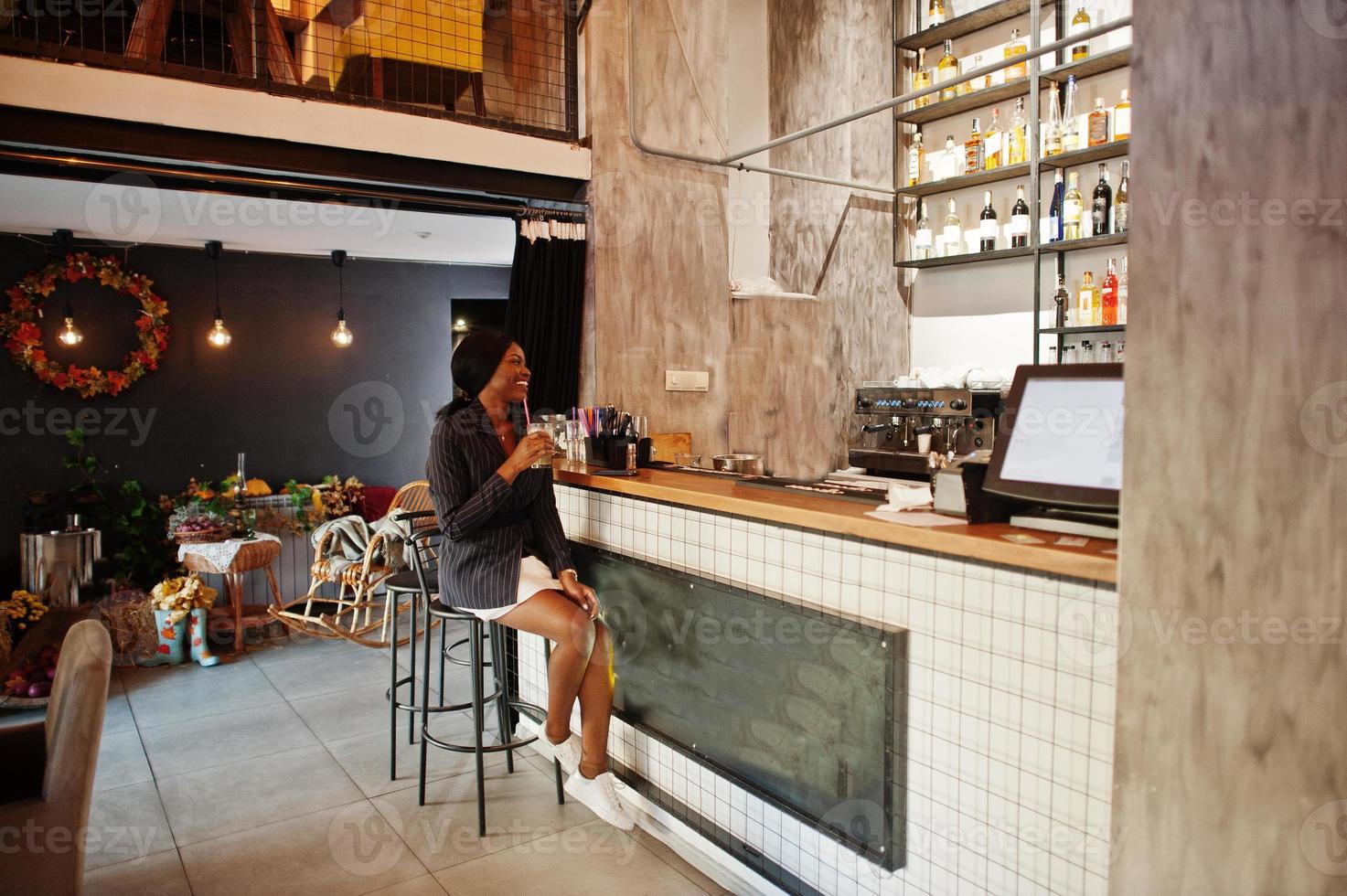 mujer de negocios afroamericana bebiendo limonada de cóctel en la cafetería del bar. chica negra descansando con teléfono móvil. foto