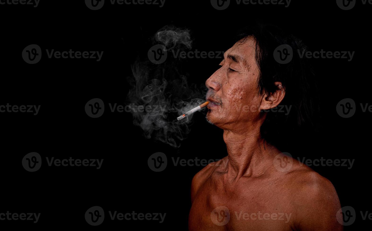 The portrait slim old man was smoking at the black background, Image of cigarette smoke spread in the mouth concept photo